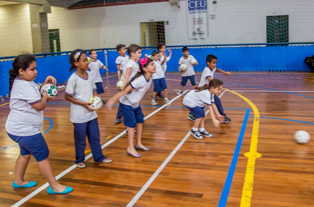 Em uma das extremidades da quadra, meninos e meninas lançam ou seguram bolas com as mãos.