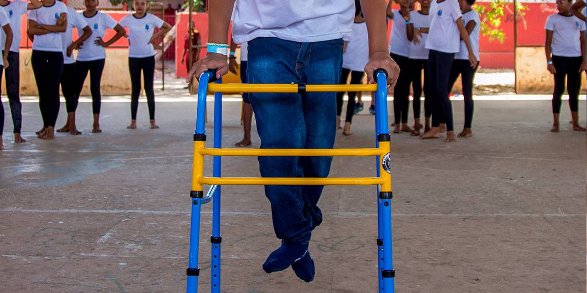 Garoto com deficiência física faz movimento de saltito apoiando-se em andador.