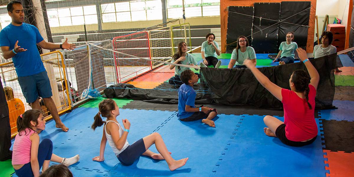 Adolescentes jogam vôlei sentado em quadra forrada por placas emborrachadas. A rede está coberta por um pano que impede que os times se vejam durante o jogo.