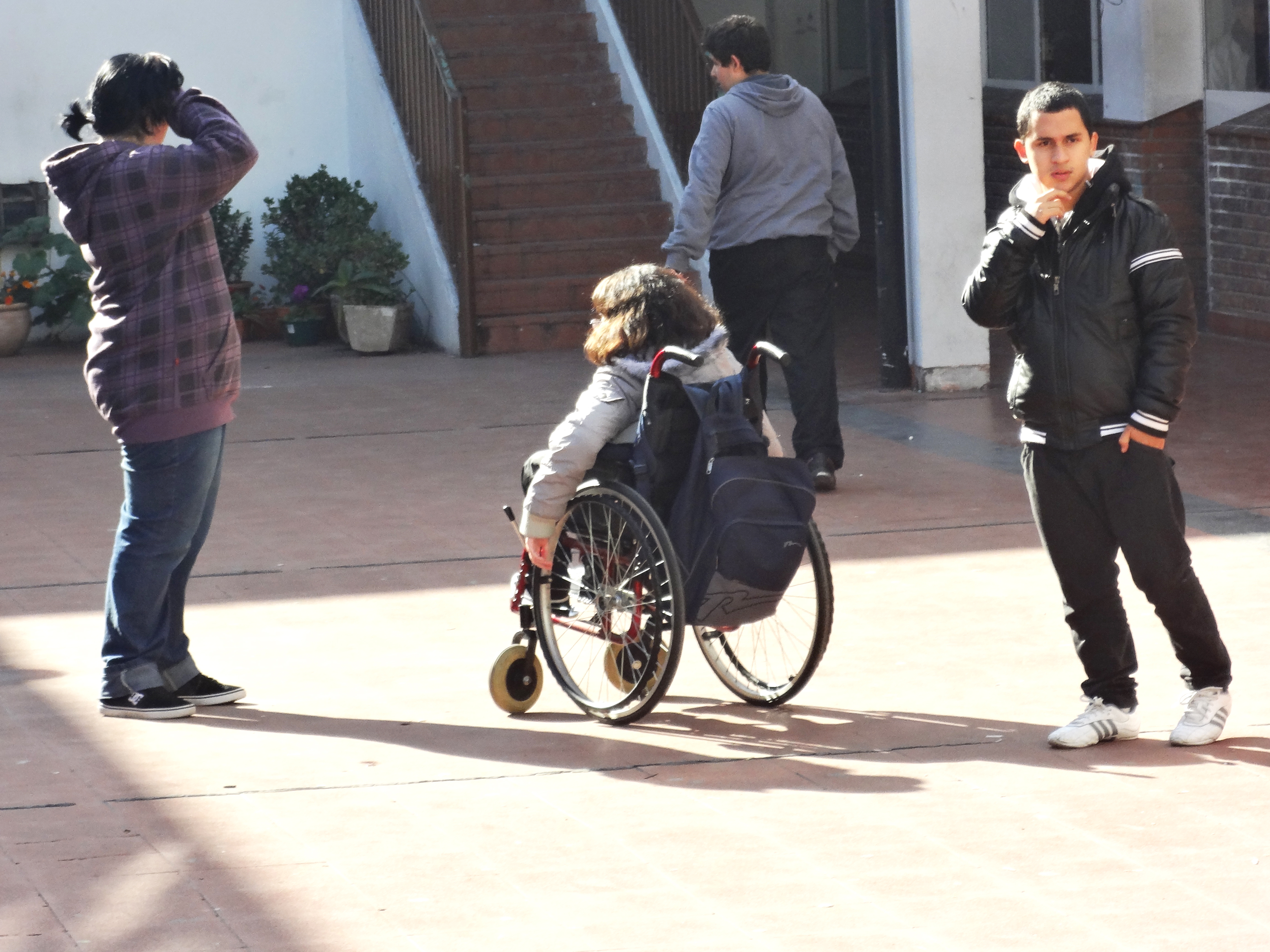 Menina em cadeira de rodas se movimenta entre outros jovens sem deficiência no pátio da escola.
