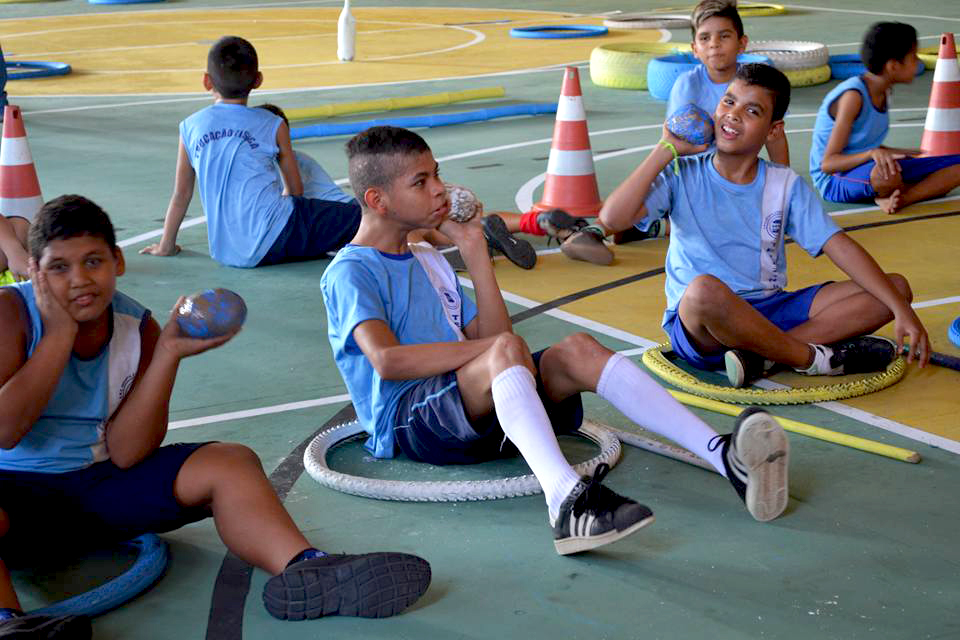 meninos sentanos em quadra escolar, se preparam para lançar bolas apoiadas em seus ombros