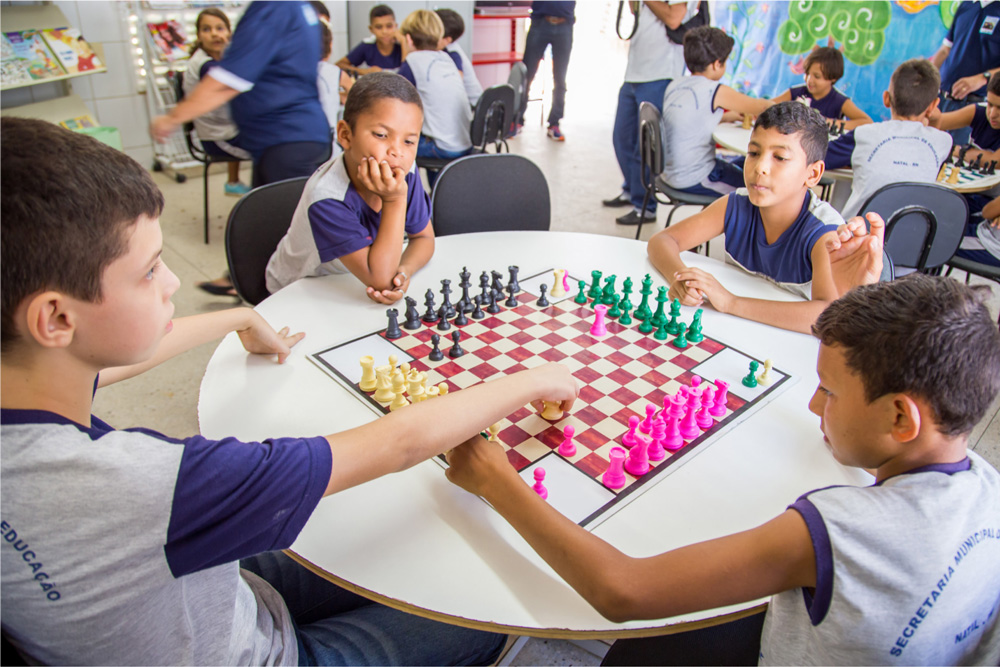 Meninos jogam xadrez em tabuleiro para quatro pessoas.