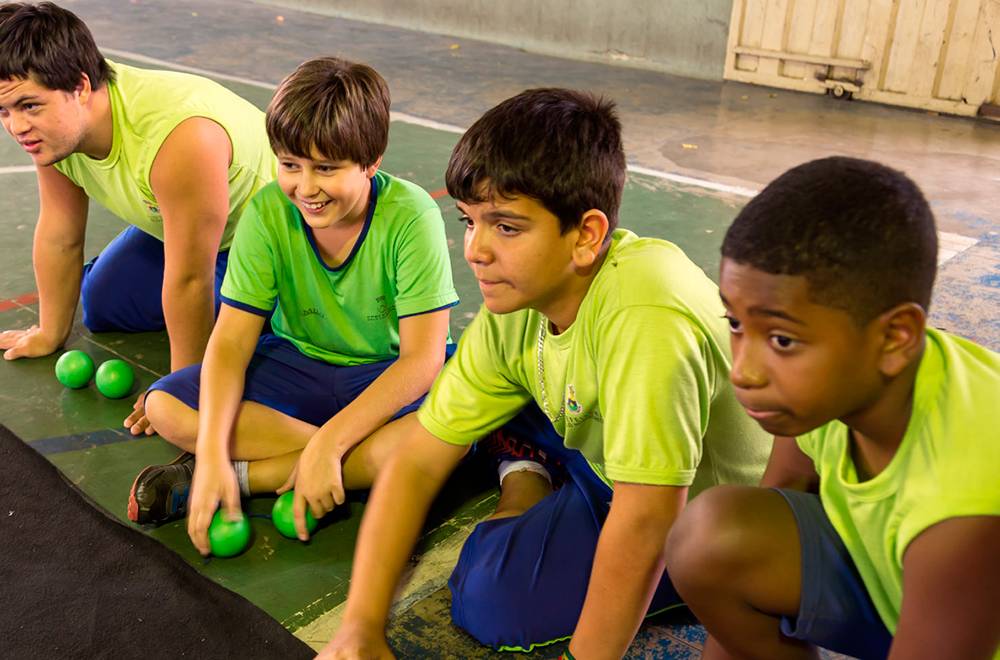 Quatro alunos sentados na extremidade do tapete, com bolas na mãos.