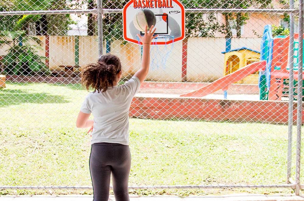 Aluna lança bola para uma cesta de basquete.