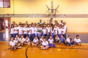 Em quadra poliesportiva, crianças com e sem deficiência e educadores posam para foto. A maioria está enfileirada em pé ao fundo, enquanto outras crianças estão sentadas no chão e em frente ao grupo.