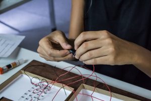 Mãos de mulher conecta fios vermelhos para formar um circuito eletrônico.