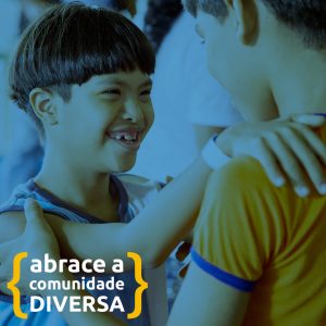 Estudante indígena com síndrome de down sorri para colega. Eles apoiam as mãos sobre o ombro um do outro. Texto: Abrace a Comunidade DIVERSA.