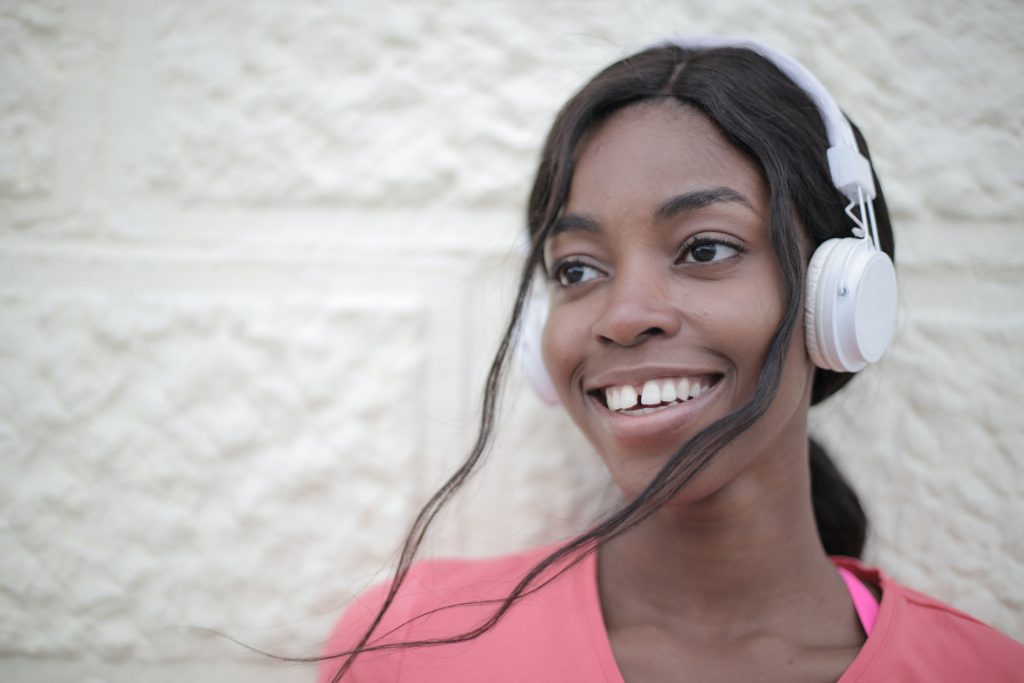 Mulher negra sorridente usa fone de ouvido e escuta áudio. Fim da descrição.

