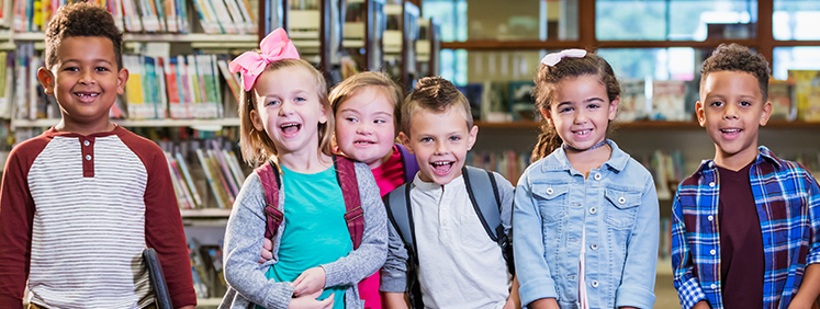 Seis crianças sorridentes posam em biblioteca escolar.