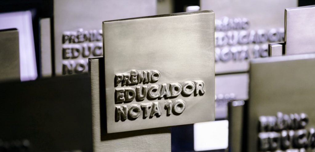 Fotografia aproximada de quatro troféus do Prêmio Educador Nota 10. Fim da descrição.
